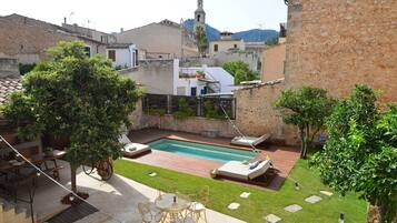 Un patio trasero con piscina, zona de comedor con mobiliario exterior y vistas a un pueblo histórico con edificios de piedra y una torre de iglesia.