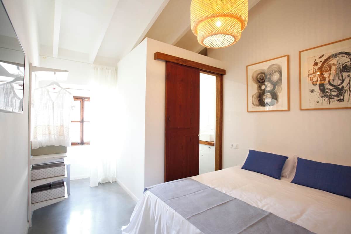 A bedroom with a bed, a wooden door, and two framed artworks on the wall.