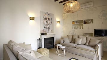 Una sala de estar con chimenea, dos sofás, un televisor y apliques decorativos en la pared.