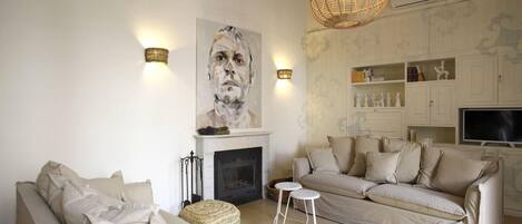 A living room with a fireplace, two sofas, a television, and decorative wall sconces.
