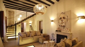 A living room with a sofa, ottoman, and a fireplace. There is a staircase leading to another level, and a painting on the wall. - Ca Sa Tieta (Alaro)