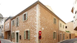 Un bâtiment en pierre avec une entrée située à l’angle, un panneau indiquant l’interdiction d’accès et une rue où se trouve une voiture rouge.
