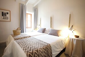 A bedroom with two beds, a window with curtains, a bedside table with a lamp, and a wall-mounted shelf. - Ca Sa Tieta (Alaro)