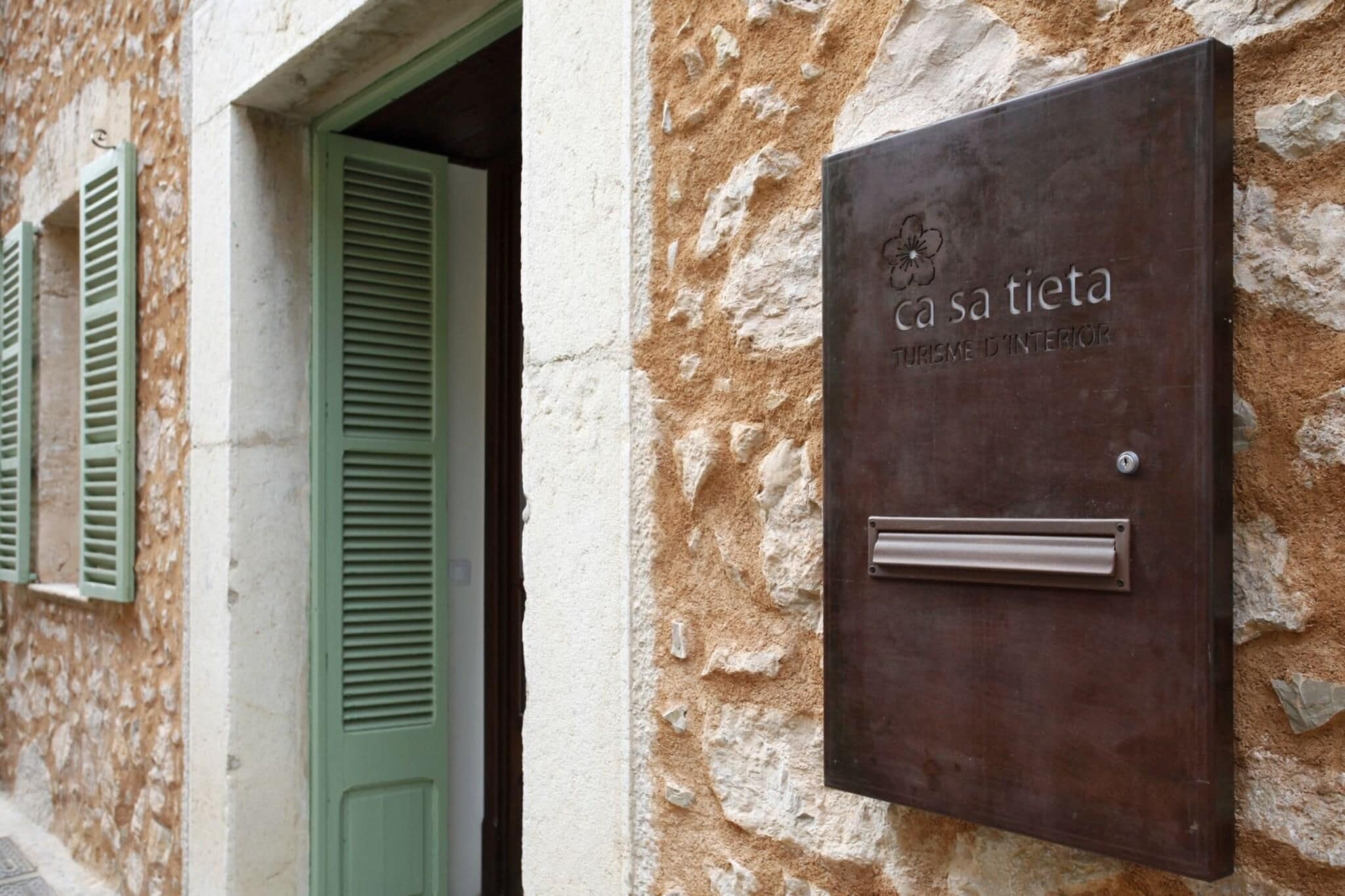 Una placa de metal con la inscripción "ca sa tieta" y "TOURME D'INTERIOR" sobre una pared de piedra texturizada.
