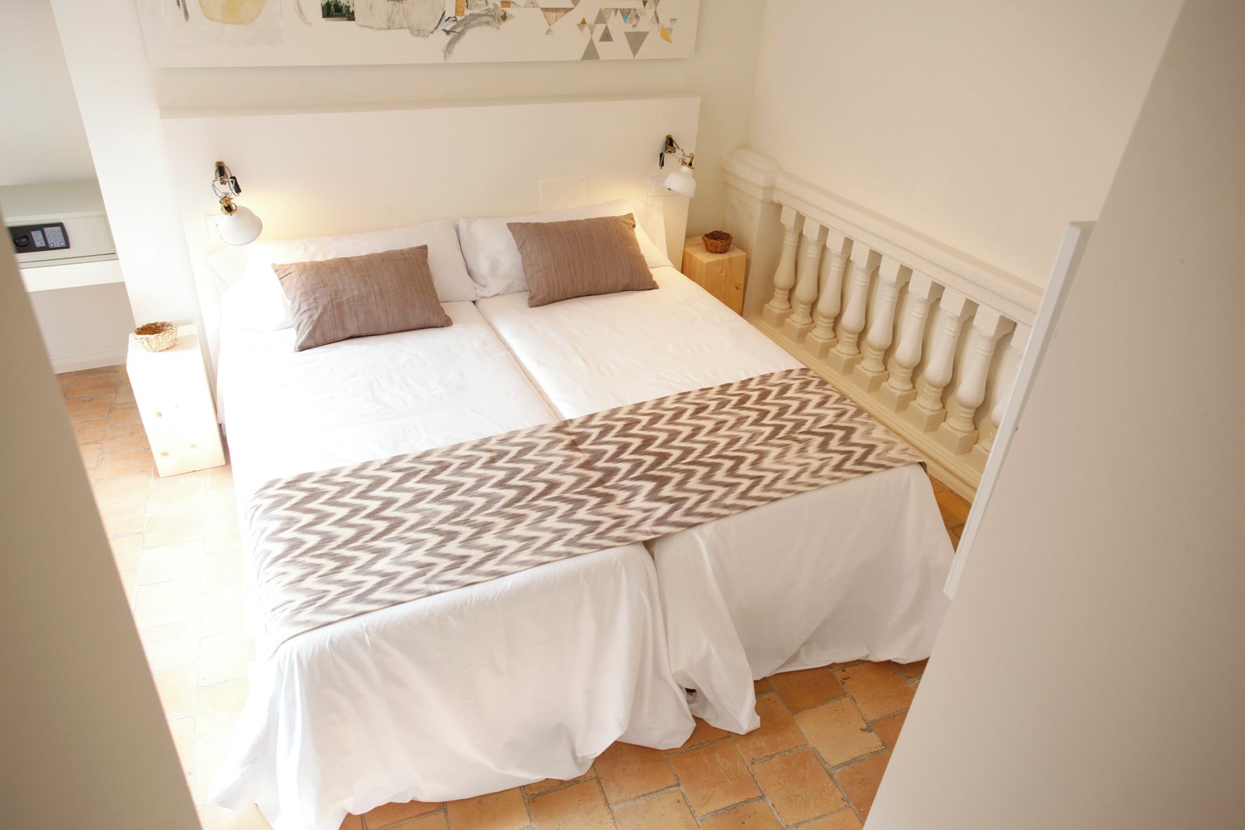 Una cama doble con una colcha estampada, dos lámparas de noche y una mesita de noche con una cesta.