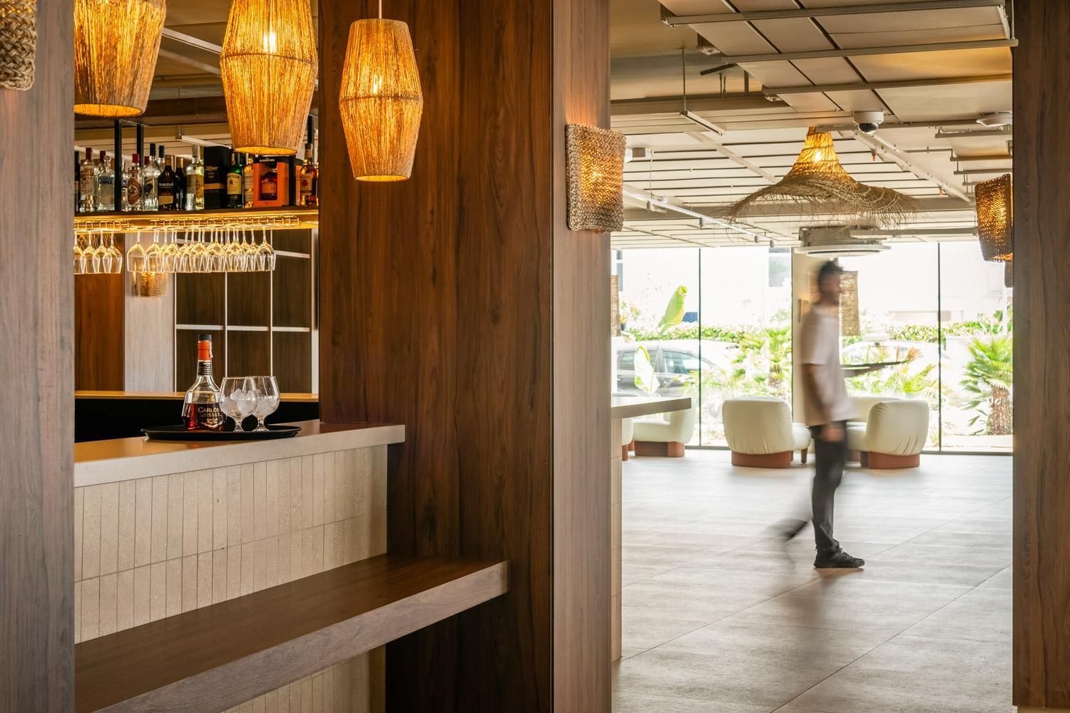 A bar area with wooden paneling, hanging wicker lamps, and a counter with glasses and bottles.