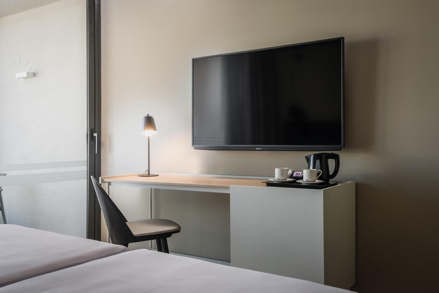 A hotel room with a bed, a desk with a lamp, a flat-screen TV, and a coffee maker.