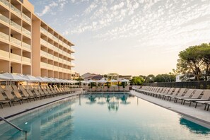 A swimming pool with lounge chairs and umbrellas, surrounded by a building with multiple balconies. - Estival Maramar (El Vendrell)