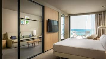 Habitación de hotel con una cama grande, televisión, sofá y balcón con vista al océano.
