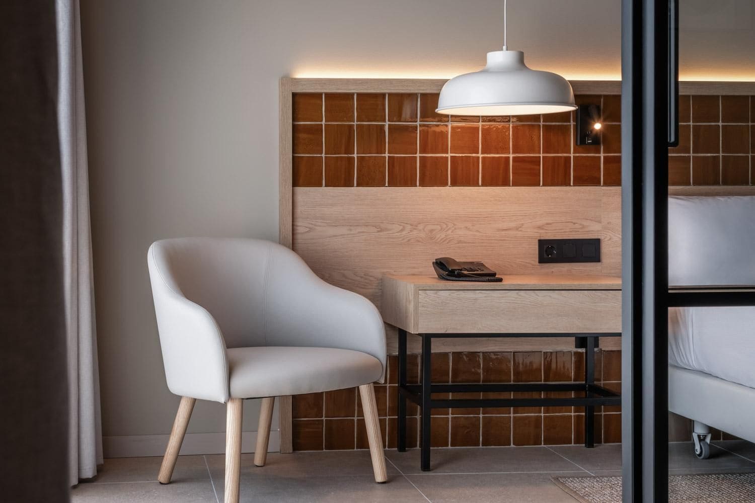 A modern room with a white chair, a wooden desk, and a white pendant light.