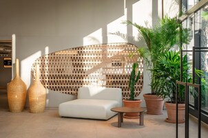 Un interior moderno con un sofá blanco, dos jarrones de mimbre, un muro de celosía de madera y plantas en macetas.