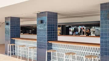 Zona de bar con taburetes altos y una barra, con columnas de azulejos azules y una máquina de café a la vista.
