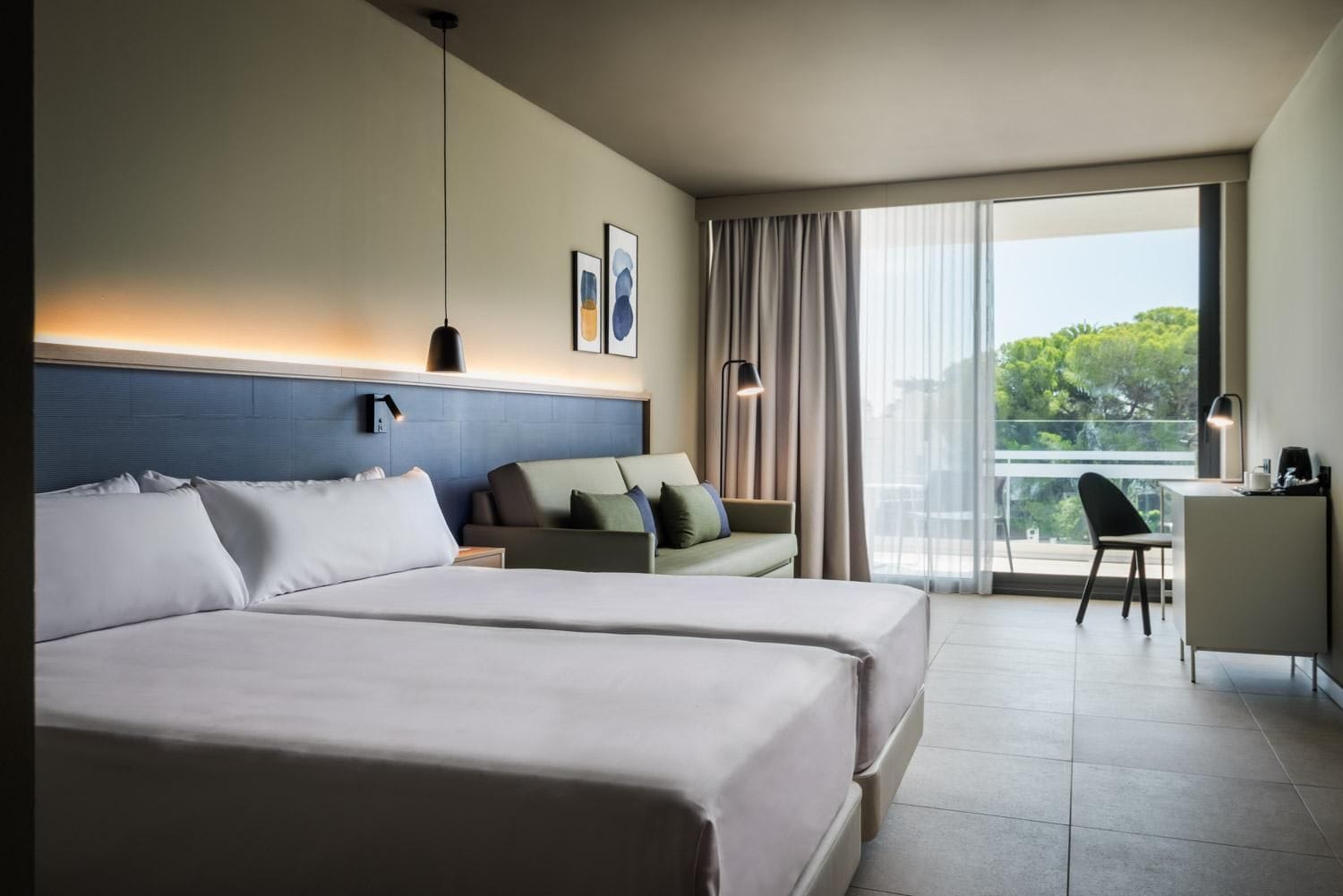 A hotel room with two beds, a desk, a chair, and a balcony with a view.