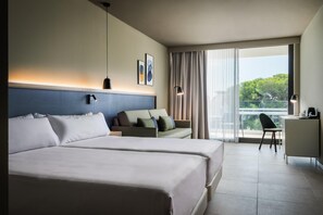 Habitación de hotel con dos camas, un escritorio, una silla y un balcón con vistas.