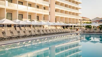 A swimming pool with lounge chairs and umbrellas, surrounded by a multi-story hotel building.