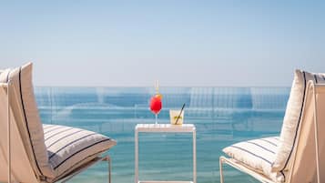 A poolside area with two lounge chairs, a small table with drinks, and a clear view of the ocean.