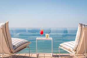 A poolside area with two lounge chairs, a small table with drinks, and a clear view of the ocean. - Estival Maramar (El Vendrell)