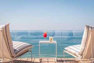 Zona junto a la piscina con dos sillones, una pequeña mesa con bebidas y vista despejada al océano.