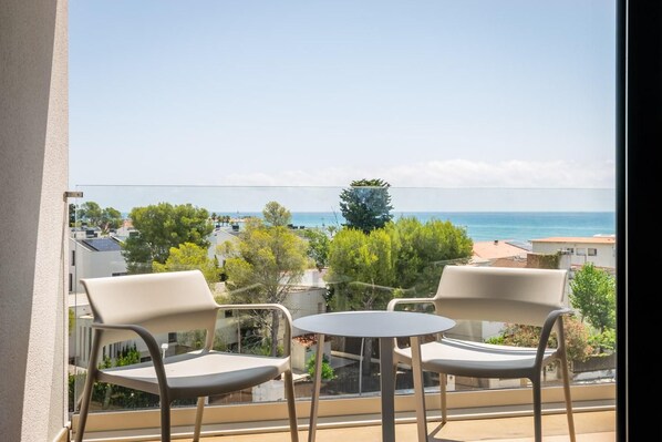 A balcony with two chairs and a small table, overlooking a coastal view with buildings and trees. - Estival Maramar (El Vendrell)