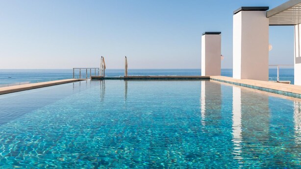 A clear blue infinity pool with a view of the ocean, white pillars, and a covered area. - Estival Maramar (El Vendrell)