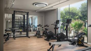 A modern gym with cardio machines, weightlifting equipment, and large windows offering a view of greenery.