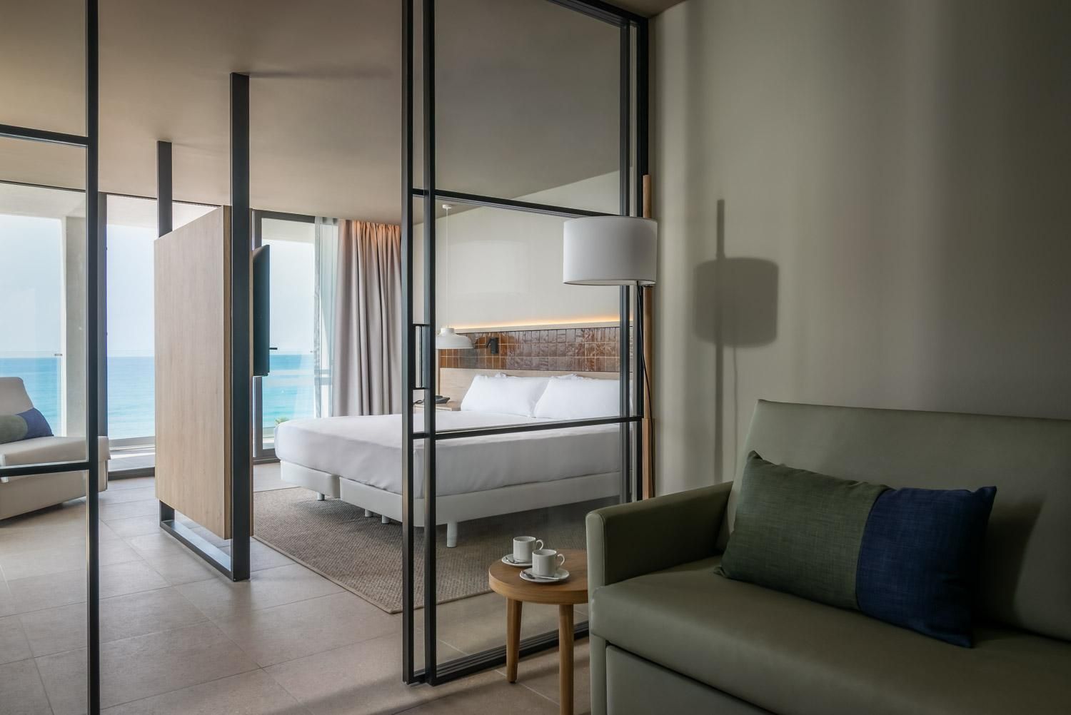 Una habitación de hotel moderna con una cama, un sofá, una mesita y vista al mar.