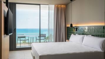 Habitación de hotel con una cama grande, televisión, balcón con vista al océano y pared de azulejos.