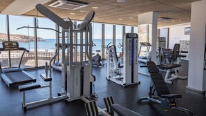 A gym with various exercise equipment, large windows overlooking a beach, and a view of the sea.