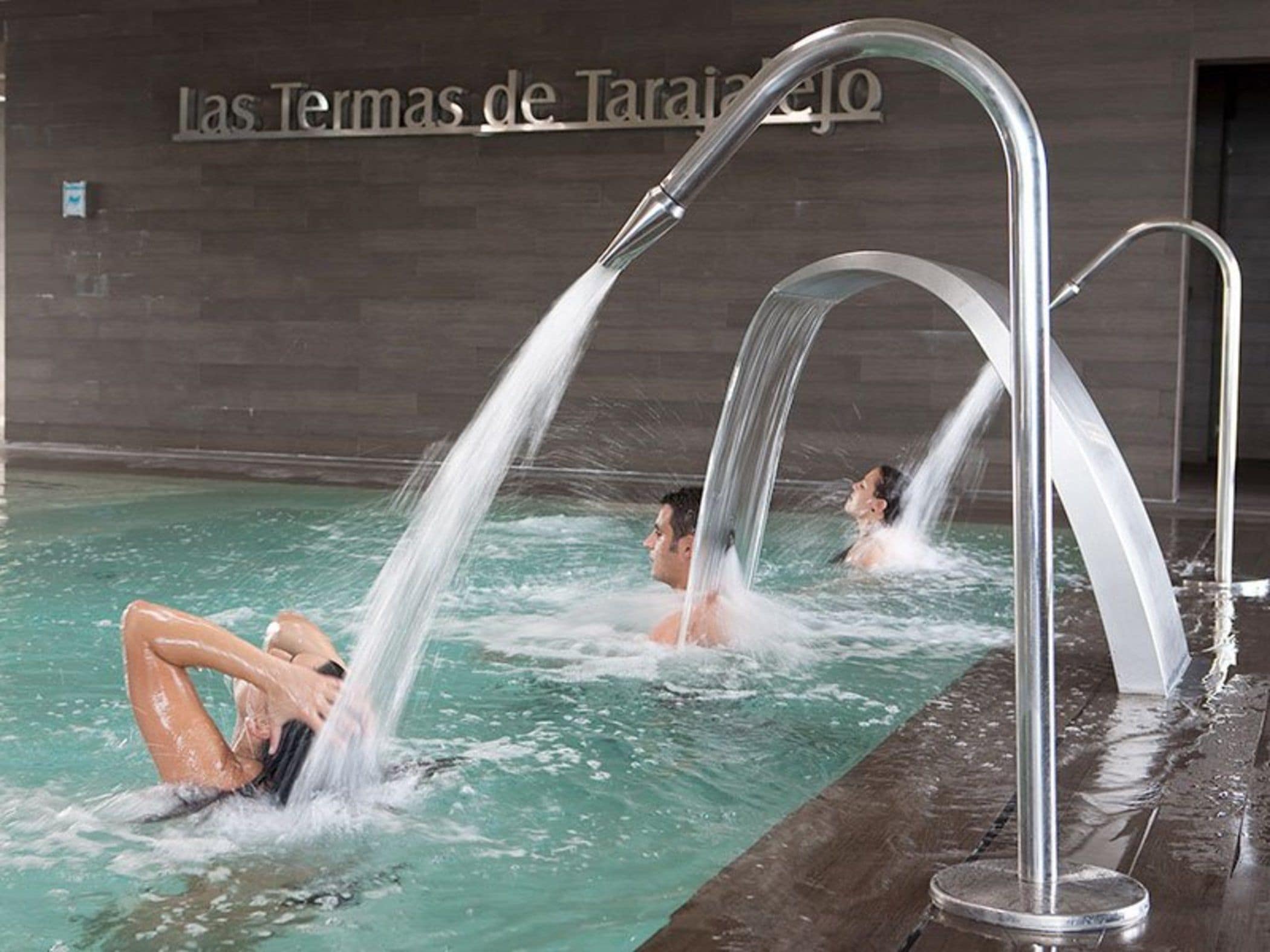A swimming pool with multiple water jets, a tiled wall with text, and a metal railing.