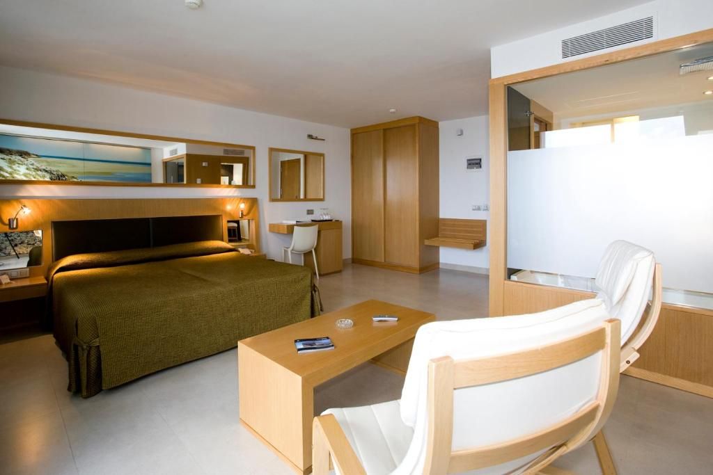 Una habitació d'hotel moderna amb un llit, una taula de treball, una cadira, un armari i un quadre a la paret.