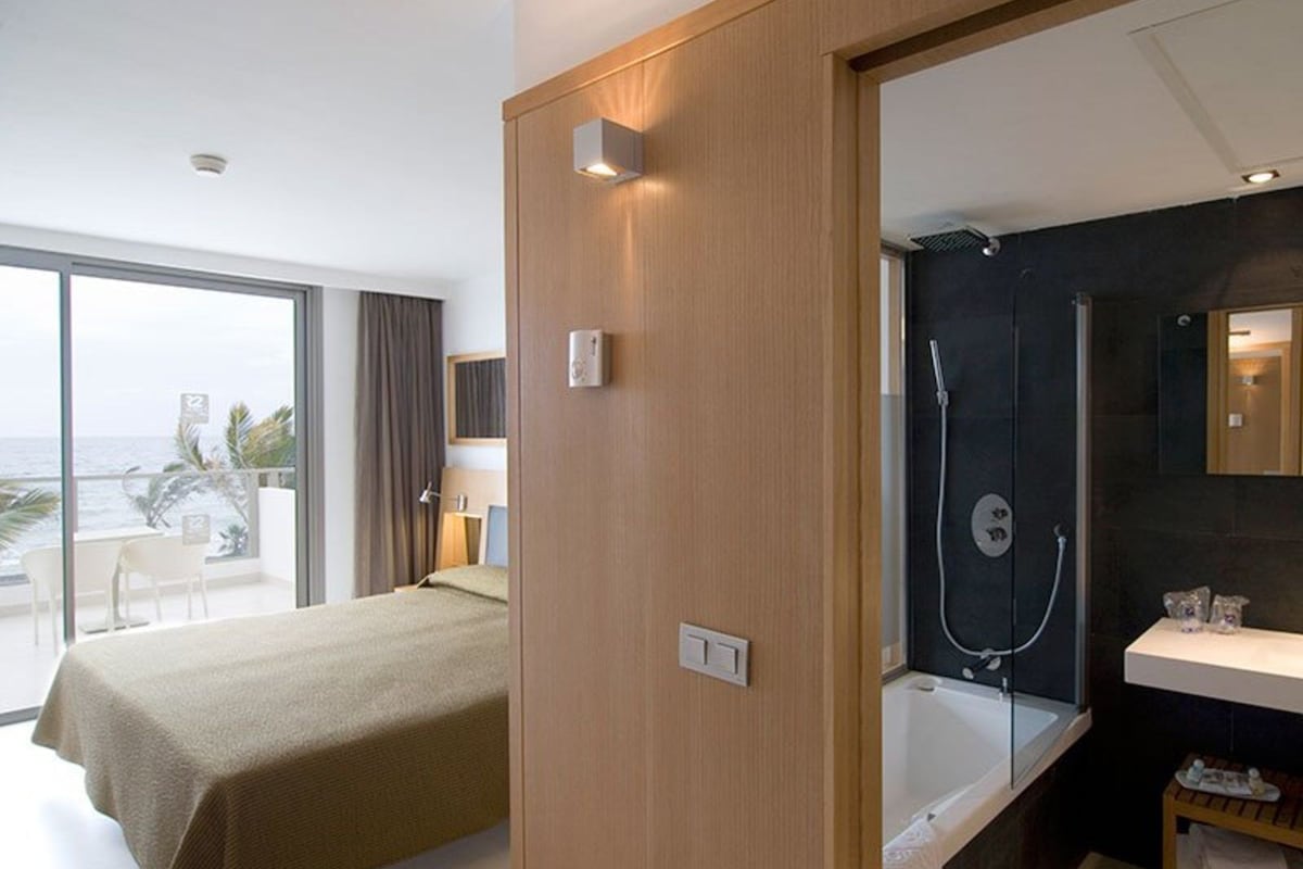Una camera d'albergo con un letto, un balcone vista mare, una doccia e un lavandino.