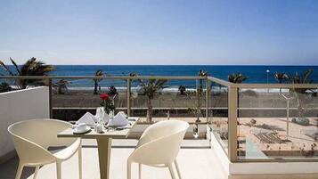 Un balcón con mesa y sillas, con vista a una playa con palmeras y el océano.