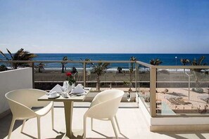 A balcony with a table and chairs, overlooking a beach with palm trees and the ocean. - R2 Bahía Design Hotel & Spa Wellness - Adults Only (Tuineje)