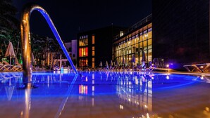 A nighttime swimming pool with a clear water surface reflecting lights, surrounded by lounge chairs and umbrellas, with a modern building in the background. - R2 Bahía Design Hotel & Spa Wellness - Adults Only (Tuineje)