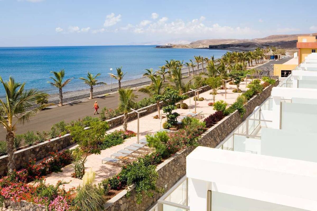 Un hôtel en bord de mer offrant une vue sur la plage, avec des palmiers et un sentier en pierre menant à la plage.