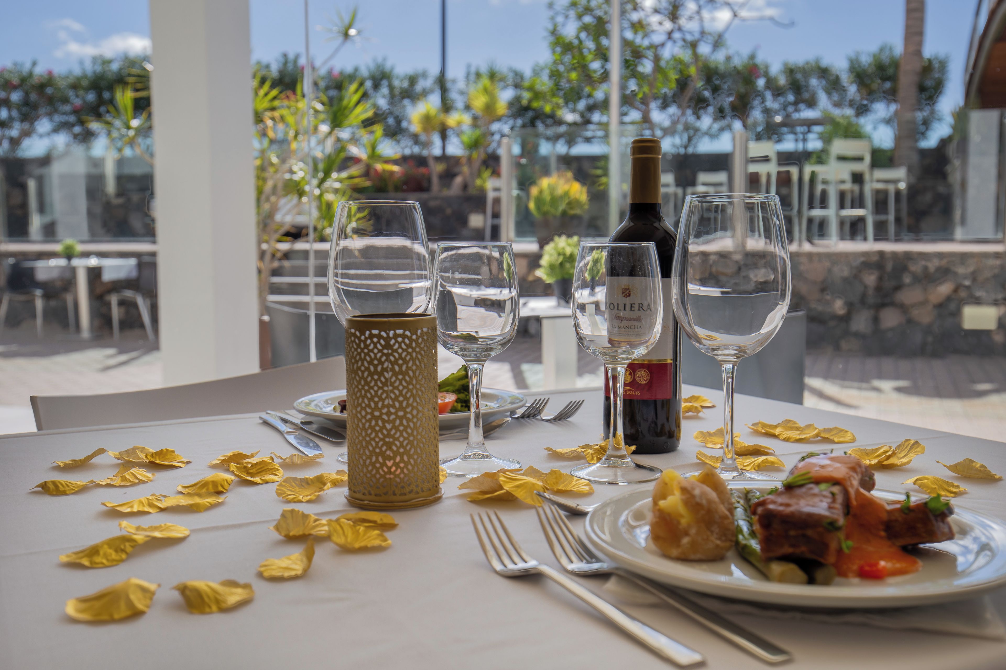 Una mesa servida para una comida, con copas de vino, una botella y un plato de comida.