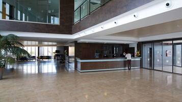 A spacious lobby with a reception desk, a large potted plant, and a glass railing overlooking the area.