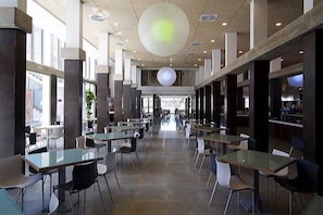 A spacious indoor area with multiple tables and chairs, large windows, and a high ceiling with a central light fixture. - R2 Bahía Design Hotel & Spa Wellness - Adults Only (Tuineje)