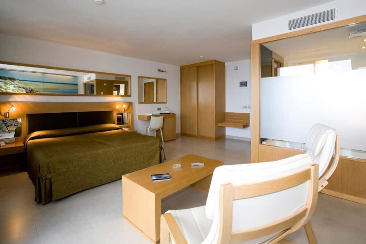 Une chambre d’hôtel moderne, équipée d’un lit, d’un bureau, d’une chaise, d’une armoire et d’un tableau au mur.