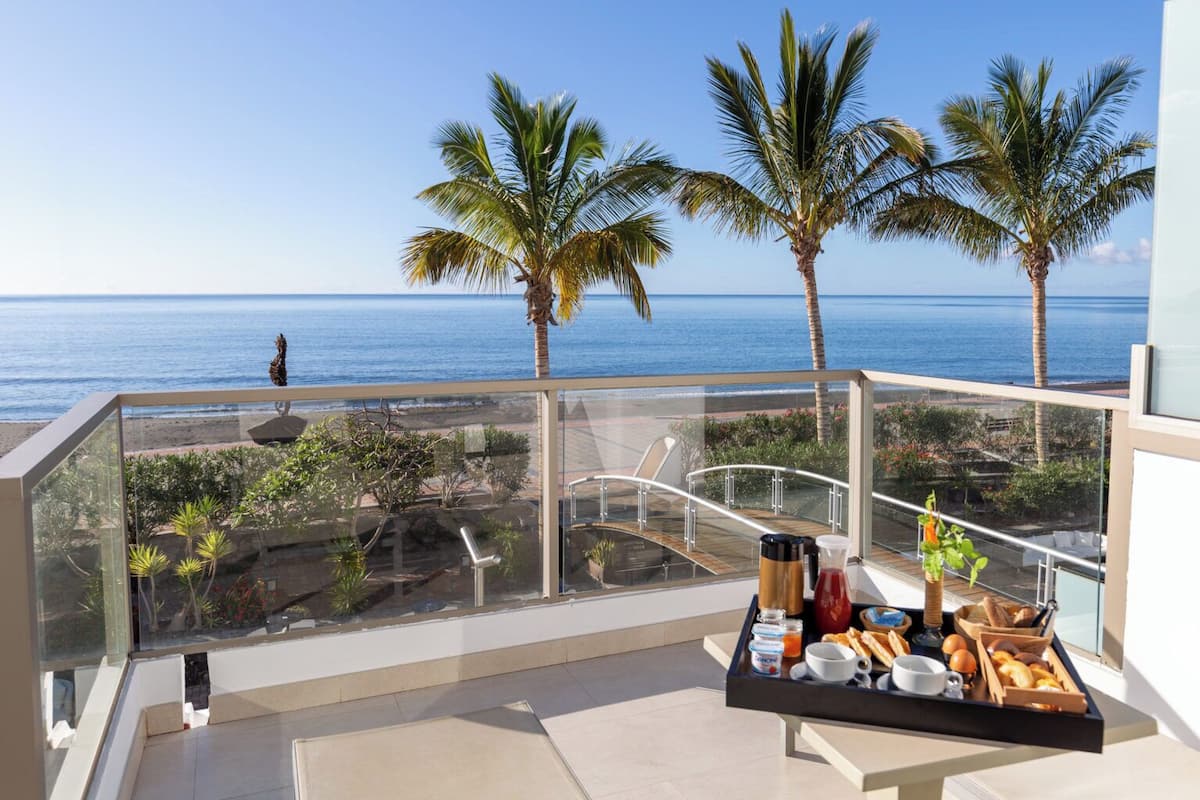 Un balcon avec un plateau de petit-déjeuner, des palmiers et une vue sur l’océan.