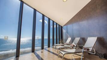 Habitación de hotel moderna con ventanas amplias que ofrecen vista al mar, una tumbona y una planta en maceta.