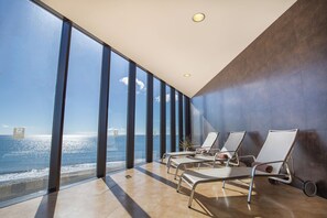 A modern hotel room with large windows offering a sea view, a sun lounger, and a potted plant. - R2 Bahía Design Hotel & Spa Wellness - Adults Only (Tuineje)