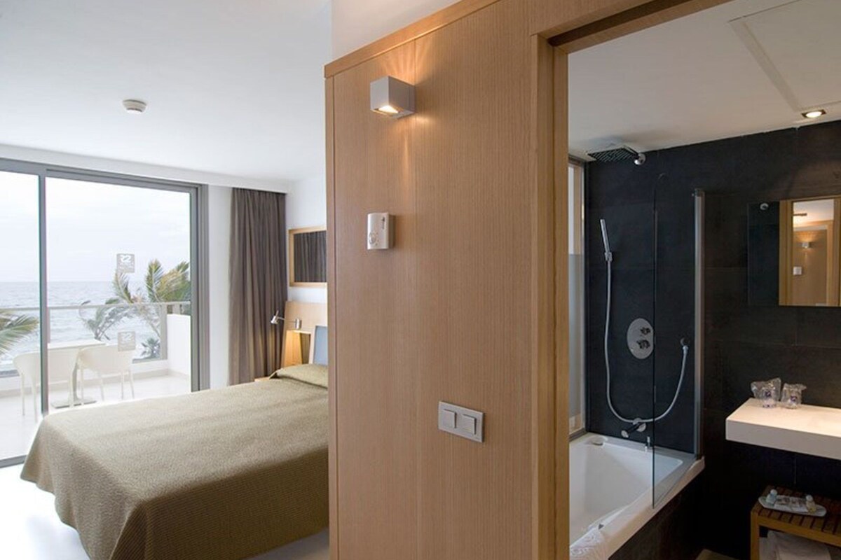 Une chambre d’hôtel avec un lit, un balcon donnant sur la mer, une douche et un lavabo.