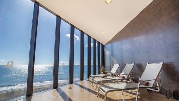 A modern hotel room with large windows offering a sea view, a sun lounger, and a potted plant. - R2 Bahía Design Hotel & Spa Wellness - Adults Only (Tuineje)
