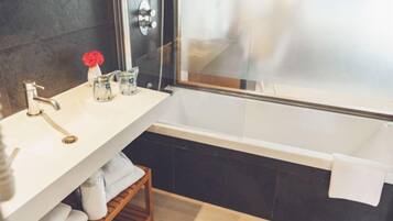 A modern bathroom with a white sink, a glass shower enclosure, and a wooden shelf with towels.