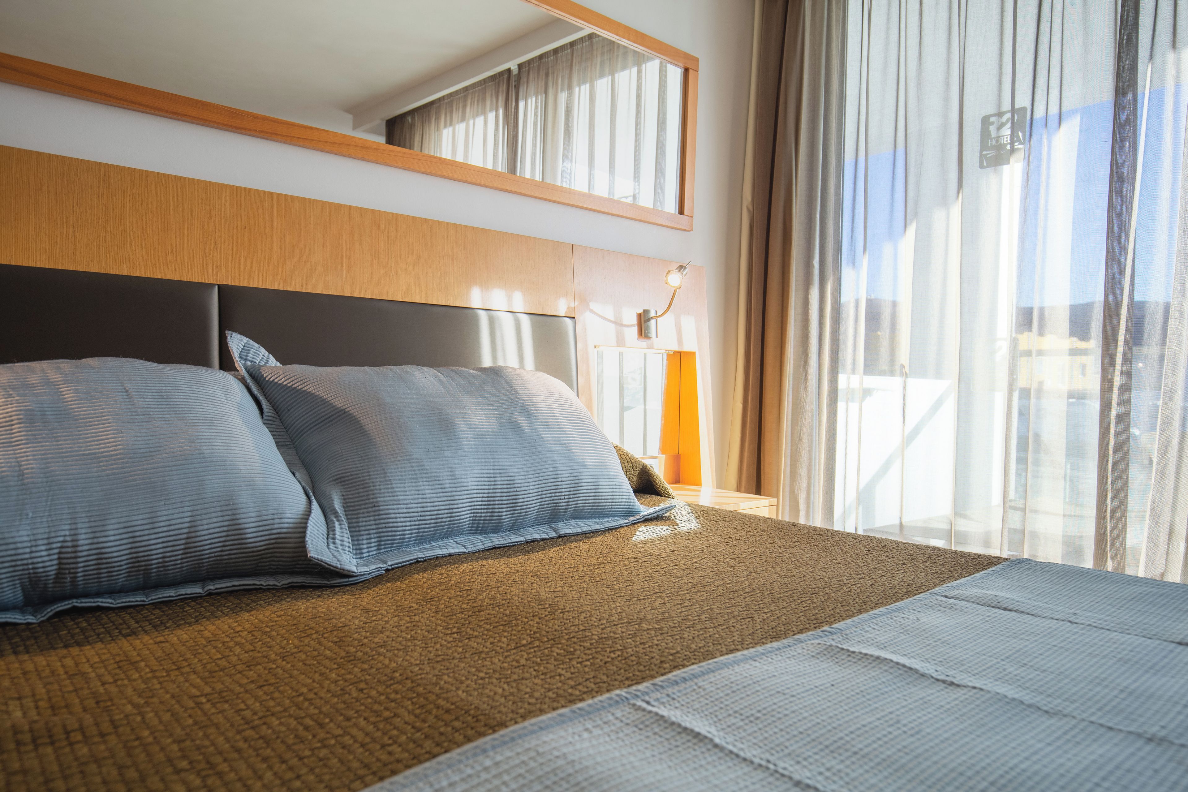 A hotel room with a large bed, a headboard, a bedside table, and a window with curtains.