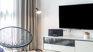 Een moderne woonkamer met een flatscreen-televisie bevestigd aan een wit kastje, een zwarte stoel en een vloerlamp.