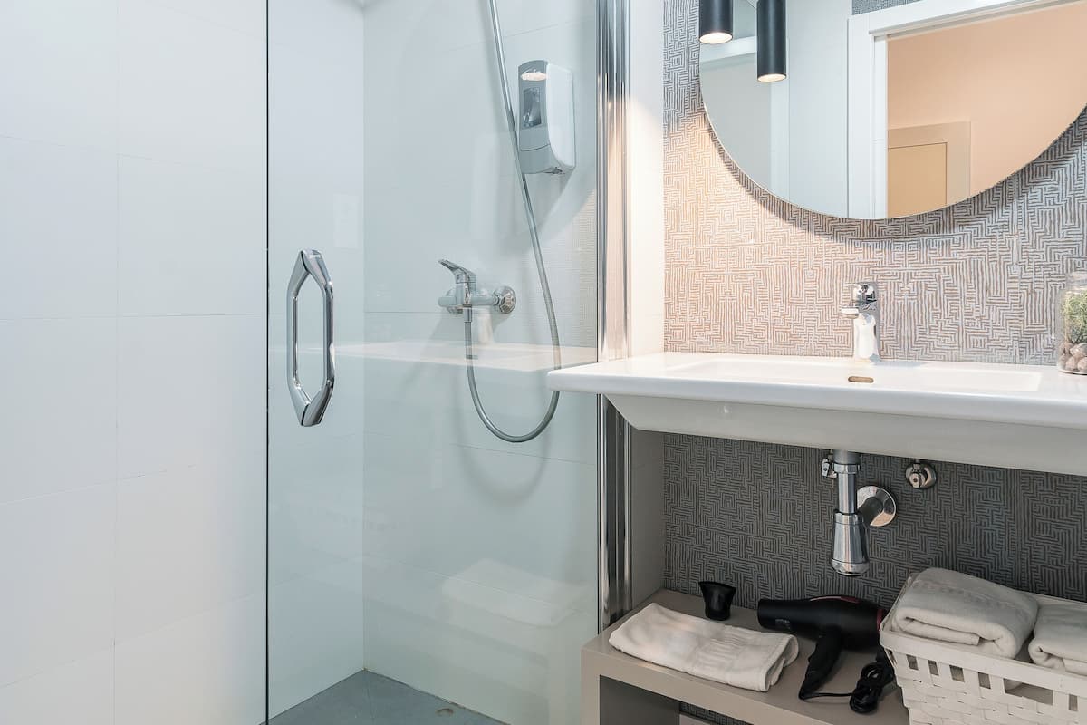 Un baño moderno con cabina de ducha de vidrio, un lavamanos blanco con un espejo encima y un salpicadero con diseño.