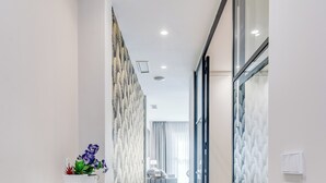 Een moderne gang met een witte plank met planten, een behang met patroon, en een zicht op een kamer met een bed en een raam.