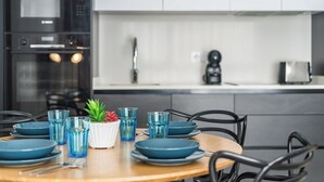 Een moderne keuken met een houten eettafel gedekt voor vier personen, met blauwe borden en glazen, en een kleine potplant.